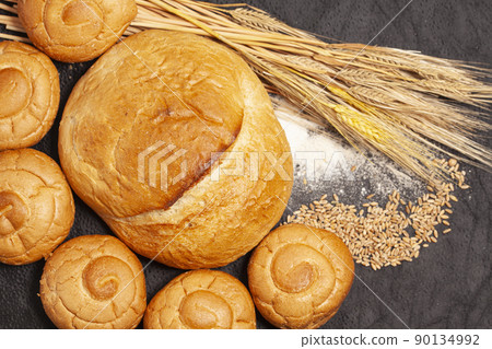 Culinary background with bread,sweet bun,wheat ears,grains on a black background, top view Culinary background with bread,sweet bun,wheat ears,grains on a black background, top view 90134992