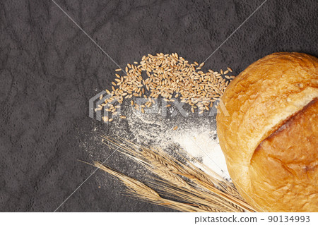 Loaf of bread with wheat ears and flour on a black background, top view Loaf of bread with wheat ears and flour on a black background, top view 90134993