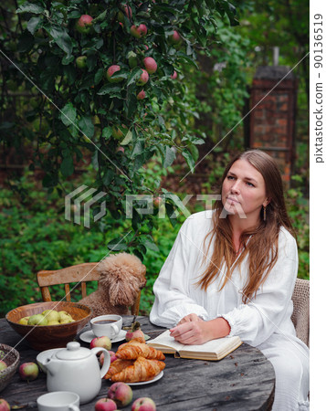 woman enjoying morning coffee in apple orchard with her pet poodle woman enjoying morning coffee in apple orchard with her pet poodle 90136519