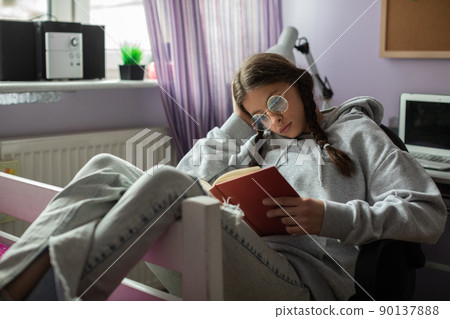 A teenage girl with braids busy reading an interesting adventure book. 90137888