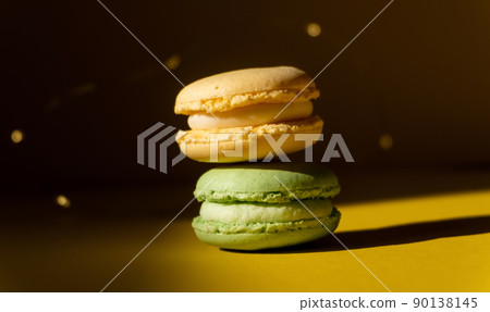 A yellow creamy macaron on top of a green one, yellow ground and dark background with yellow sparkles 90138145
