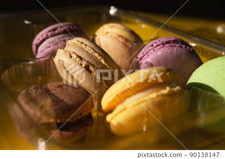 Set of multiple colorful macarons in a plastic container, yellow background and sparkles in the dark Set of multiple colorful macarons in a plastic container, yellow background and sparkles in the dark 90138147