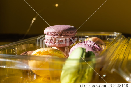 Set of multiple colorful macarons in a plastic container, yellow background and sparkles in the dark Set of multiple colorful macarons in a plastic container, yellow background and sparkles in the dark 90138148