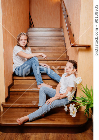 two brothers of a teenager in white T-shirts and jeans on a wooden staircase  90139935