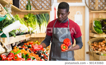 Salesman filling counter with vegetables and fruits 90143060