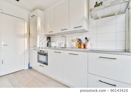 Fragment of interior of light narrow home kitchen with minimalist style white furniture with sink and stove 90143428