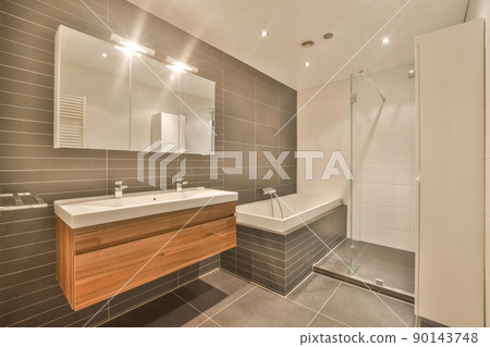 The interior of a modern bathroom with a double ceramic sink and a bathtub and shower in a modern house The interior of a modern bathroom with a double ceramic sink and a bathtub and shower in a modern house 90143748