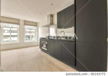 A spacious empty room in bright colors with large windows and a small kitchen in a dark color in a cozy apartment 90143775
