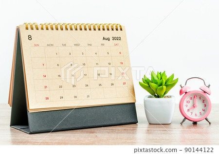 August 2022 green Desk calendar with pink alarm clock on wooden table. August 2022 green Desk calendar with pink alarm clock on wooden table. 90144122