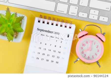 September 2022 desk calendar and pink alarm clock on yellow background. September 2022 desk calendar and pink alarm clock on yellow background. 90144124