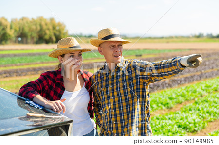 Positive woman and man standing near car and pointing to something 90149985