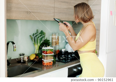 A slender blogger girl takes a photo of vegetables on her phone in the kitchen. The concept of a healthy diet and a healthy lifestyle. A slender blogger girl takes a photo of vegetables on her phone in the kitchen. The concept of a healthy diet and a healthy lifestyle. 90152961