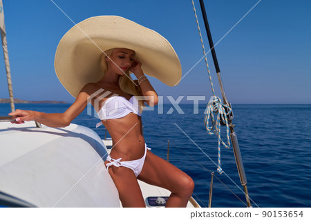 Beautiful young blond woman in bikini standing on catamaran at sunny summer day 90153654