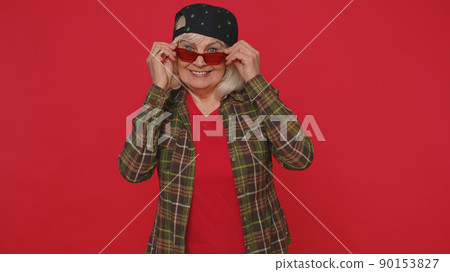 Seductive cheerful stylish mature old woman in shirt wearing sunglasses, charming smile on pink wall Seductive cheerful stylish mature old woman in shirt wearing sunglasses, charming smile on pink wall 90153827