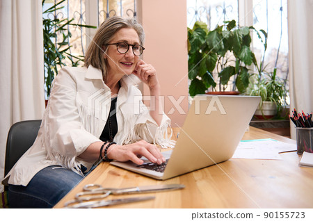 Mature elegant grey-haired European woman fashion designer, small business owner, thinking on new creative ideas at workplace in tailoring atelier Mature elegant grey-haired European woman fashion designer, small business owner, thinking on new creative ideas at workplace in tailoring atelier 90155723