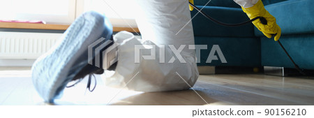A man in a protective suit sprays under the couch A man in a protective suit sprays under the couch 90156210