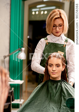 Professional hair care. Beautiful young caucasian brunette woman with long hair receiving hairstyling in a beauty salon Professional hair care. Beautiful young caucasian brunette woman with long hair receiving hairstyling in a beauty salon 90156368