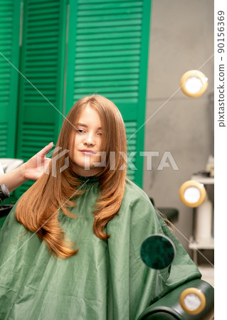 Professional hair care. Young female red-haired with long hair receiving hairstyling in a beauty salon. Professional hair care. Young female red-haired with long hair receiving hairstyling in a beauty salon. 90156369