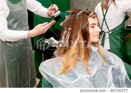 A female hairdresser dyes the hair of a young Caucasian woman with a brush and foil in a beauty salon 90156377