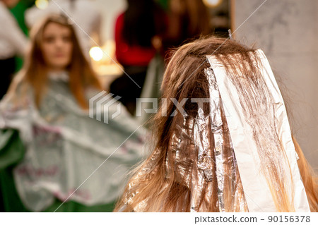 Beautiful young caucasian woman with foil in her hair while dyeing her hair sitting in a beauty salon Beautiful young caucasian woman with foil in her hair while dyeing her hair sitting in a beauty salon 90156378