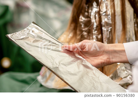 Hairdresser's Hands Holding Foil Sheet For Hair Dye In Beauty Salon Hairdresser's Hands Holding Foil Sheet For Hair Dye In Beauty Salon 90156380
