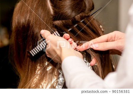 Hairdresser's hands prepare brown hair for dyeing with a comb and foil in a beauty salon, close up Hairdresser's hands prepare brown hair for dyeing with a comb and foil in a beauty salon, close up 90156381