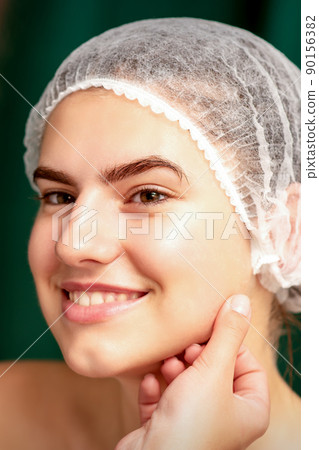 Plastic surgery and beauty concept. Professional cosmetician examining and touching the face of the beautiful young caucasian smiling woman in a clinic of esthetic cosmetology 90156382