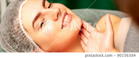Plastic surgery and beauty concept. Professional cosmetician examining and touching the face of the beautiful young caucasian smiling woman in a clinic of esthetic cosmetology Plastic surgery and beauty concept. Professional cosmetician examining and touching the face of the beautiful young caucasian smiling woman in a clinic of esthetic cosmetology 90156384