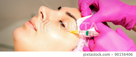The young white woman is getting rejuvenating facial injections with hyaluronic acid on the eye in a beauty clinic The young white woman is getting rejuvenating facial injections with hyaluronic acid on the eye in a beauty clinic 90156406
