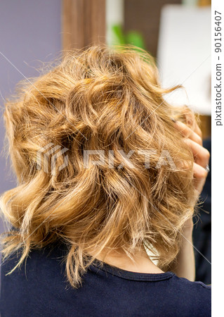 Rear view of young woman checking her new curly brown hairstyle at the hairdresser salon 90156407