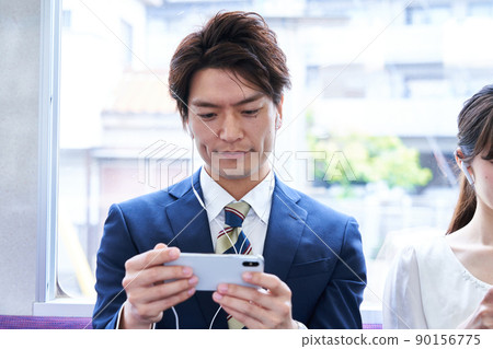 A man in a suit looking at a smartphone on the train Photo cooperation "Keio Electric Railway Co., Ltd." A man in a suit looking at a smartphone on the train Photo cooperation "Keio Electric Railway Co., Ltd." 90156775