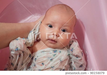 Mother splashes water on little baby washing in pink bath Mother splashes water on little baby washing in pink bath 90158079