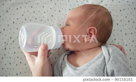 Newborn baby drinks water from plastic bottle lying on bed Newborn baby drinks water from plastic bottle lying on bed 90158101