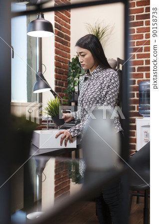 Dismissed company employee putting her things in a cardboard box after being left jobless. Upset project manager taking home personal objects after briefing about being fired from company workplace. 90158738