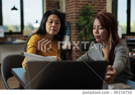 Asian entrepreneurs working at marketing project analyzing statistics on laptop computer brainstorming ideas during business meeting in startup office. Executive managers collaborating together 90158750