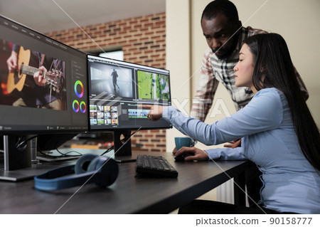 Professional digital movie editor sitting at desk while improving film frames and improving footage quality. Post production house team leader talking with coworker about quality of frames. Professional digital movie editor sitting at desk while improving film frames and improving footage quality. Post production house team leader talking with coworker about quality of frames. 90158777