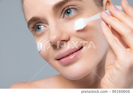 Portrait of tender beautiful woman taking care after skin, applying moisturizing cream isolated on grey studio background. Close-up Portrait of tender beautiful woman taking care after skin, applying moisturizing cream isolated on grey studio background. Close-up 90160608