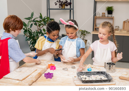 Happy cute boy with raw selfmade cookies looking at you while standing by kitchen table in front of camera 90160893
