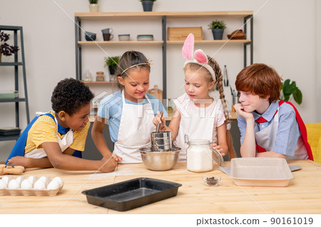 Children wearing apron browsing Internet on digital tablet in order to find recipe of appetizing cookie Children wearing apron browsing Internet on digital tablet in order to find recipe of appetizing cookie 90161019