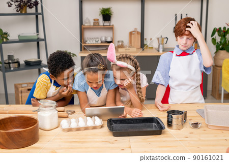 Little food blogger wearing apron working on new video and explaining her followers how to prepare food, spacious kitchen on background Little food blogger wearing apron working on new video and explaining her followers how to prepare food, spacious kitchen on background 90161021