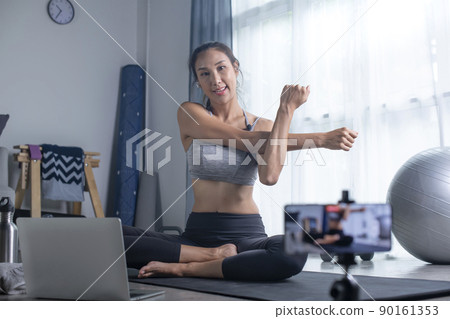 Asian woman using phone camera for live streaming teach yoga online in living room Asian woman using phone camera for live streaming teach yoga online in living room 90161353