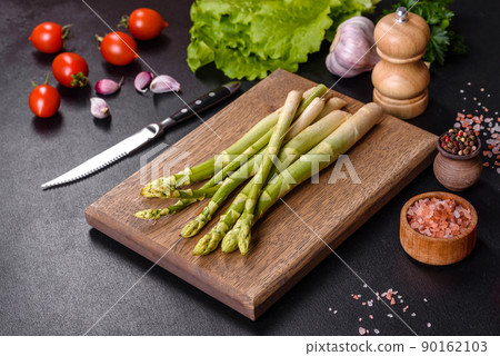 A bunch of branches of fresh green raw asparagus on a wooden cutting board A bunch of branches of fresh green raw asparagus on a wooden cutting board 90162103