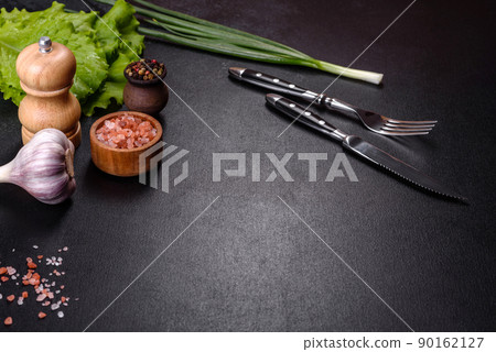 Fork, knife, spices and herbs, cutting board on a dark concrete background Fork, knife, spices and herbs, cutting board on a dark concrete background 90162127