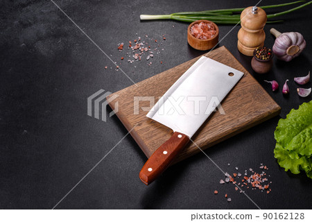 An axe for meat, spices and herbs, a cutting board against a dark concrete background 90162128
