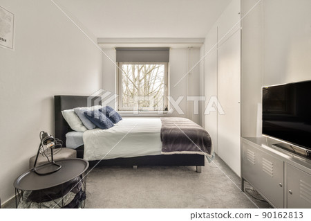 The interior of a bedroom with a gray and white design and a large window in a cozy apartment The interior of a bedroom with a gray and white design and a large window in a cozy apartment 90162813