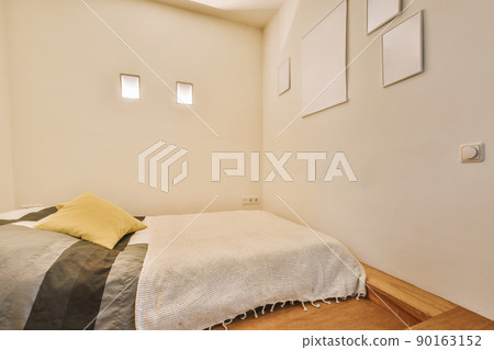 Comfortable low bed placed in small narrow minimalist style bedroom with white walls, pictures and small windows in modern apartment Comfortable low bed placed in small narrow minimalist style bedroom with white walls, pictures and small windows in modern apartment 90163152
