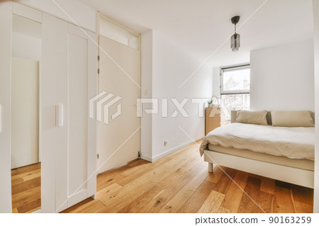Home interior design of bedroom with bed and wooden wardrobe placed in corner near window in modern apartment 90163259