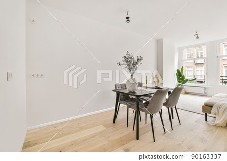 Shabby wooden table with chairs and vase located near comfortable couch against light walls with decorations in modern apartment 90163337