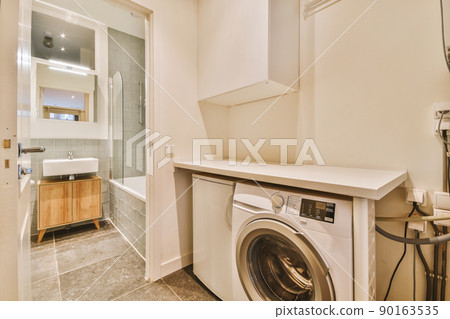 A cozy bathroom with a ceramic sink, washing machine and a bathtub with a glazed shower in a modern house 90163535