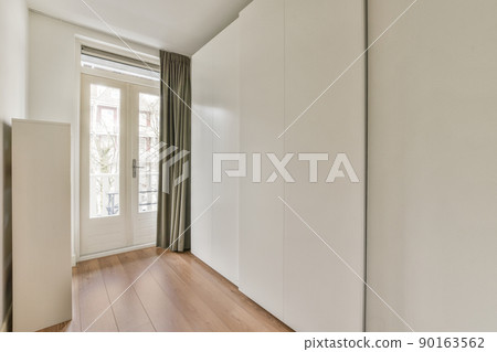 Modern cupboard and vintage chest placed near doors and wicker basket in spacious room with white walls and wooden floor 90163562